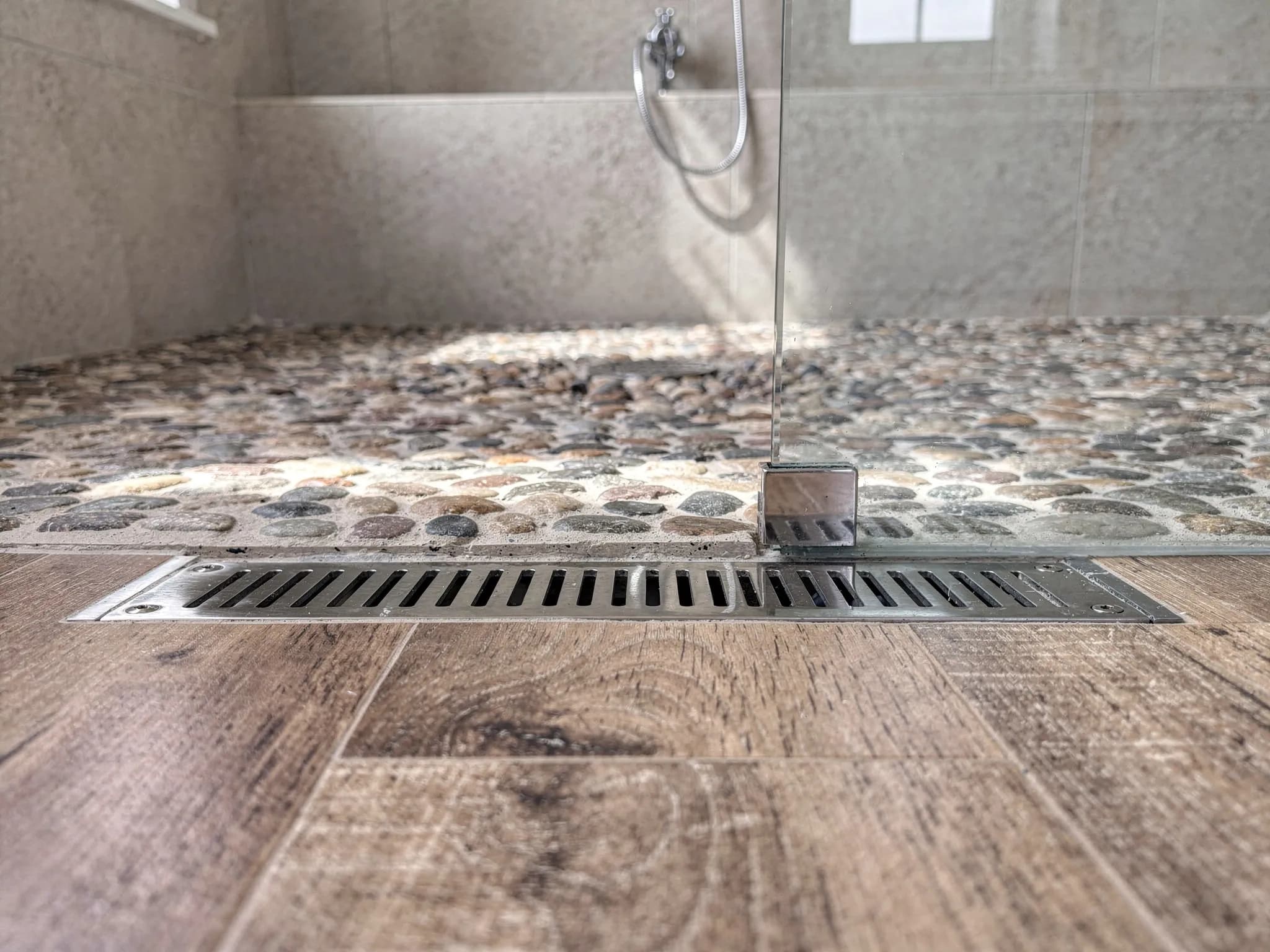 A curbless shower entry with a linear drain — wood-look tile flowing in without a single trip point.